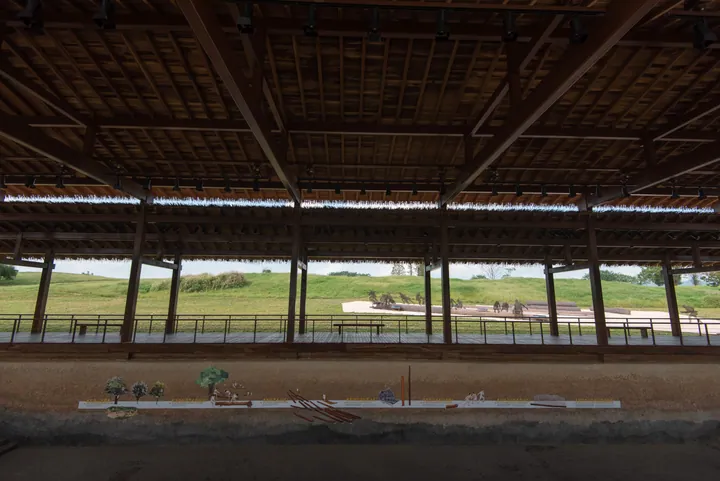Wooden roofed structure over grassy excavated earthen mounds with interpretive models