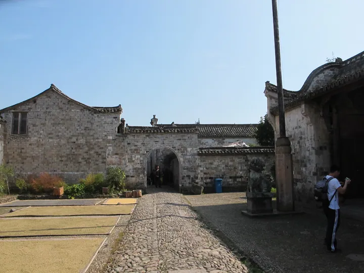 Stone archway leading into an old village courtyard with traditional tiled-roof buildings