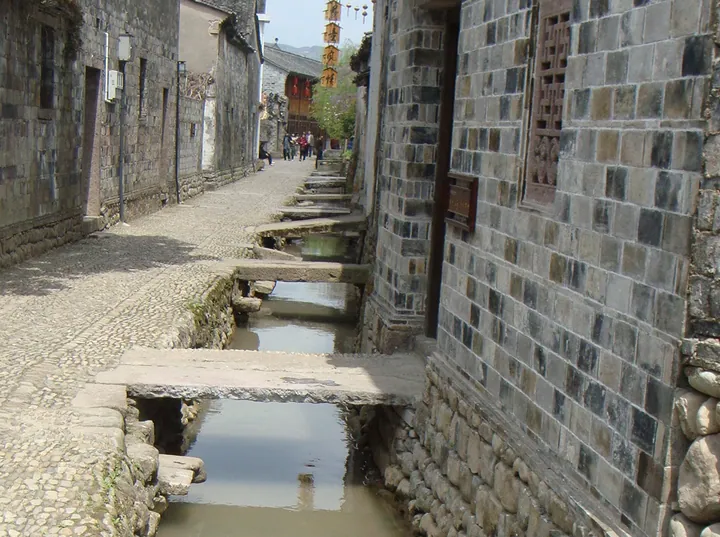 A narrow stone street beside a small water channel lined with old houses