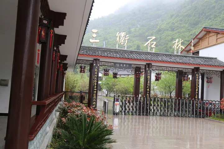 Traditional Chinese gate building with the name Sanqu Shilin carved above the entrance, misty green hills behind