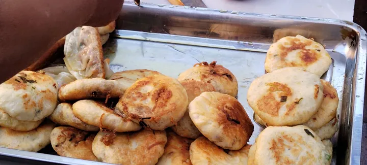 A tray of golden pan-fried flatbread cakes at a street food stall