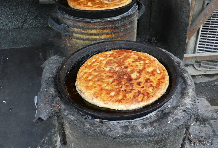 Golden fried beef-filled flatbread cooking on a round street-stall griddle
