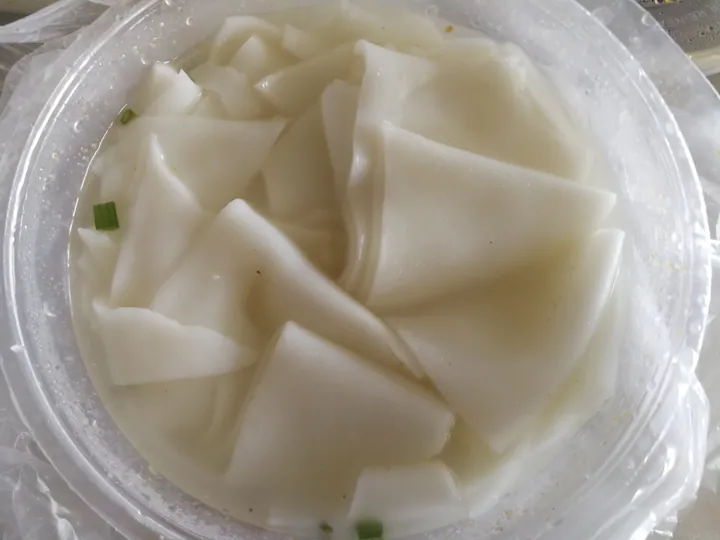Bowl of cooked flat rice noodle strips (guo tiao) with scallions.