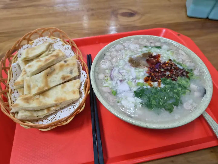 Bowl of meat-and-broth soup with herb garnish, served beside a basket of fried flatbread