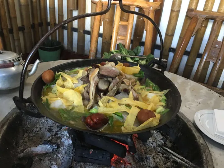 A hanging iron pot of stewed meat and vegetables simmering over charcoal