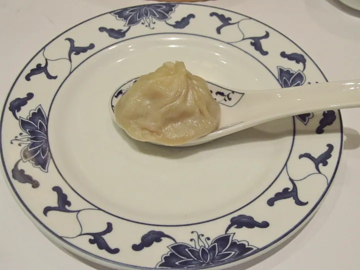 A single translucent soup dumpling resting on a Chinese soup spoon.