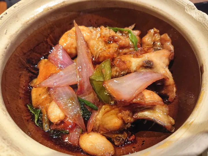 Braised three-cup chicken in a clay pot with ginger and scallions.