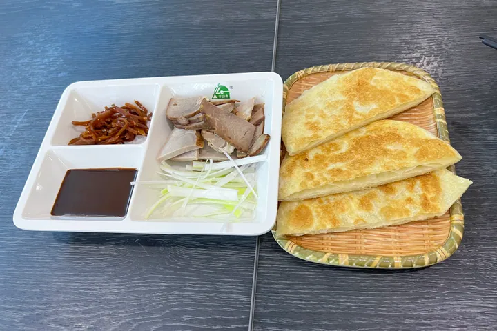 Sliced smoked pork, scallion shreds, dipping sauce and folded pan-fried flatbread on a woven tray