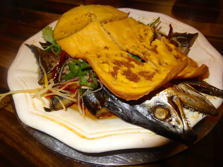 Plate of salted fish with a golden fried corn cake on top, garnished with chili and herbs