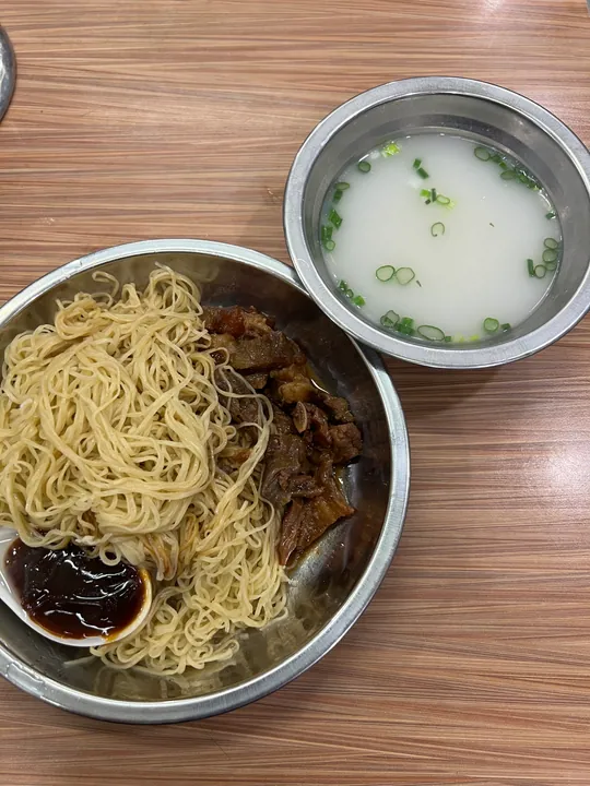 A bowl of thin yellow bamboo-pressed noodles with braised beef and a side bowl of broth