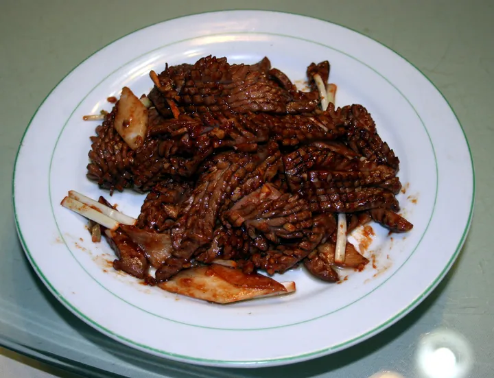 A plate of scored, stir-fried sliced pork kidney with scallion on a white plate