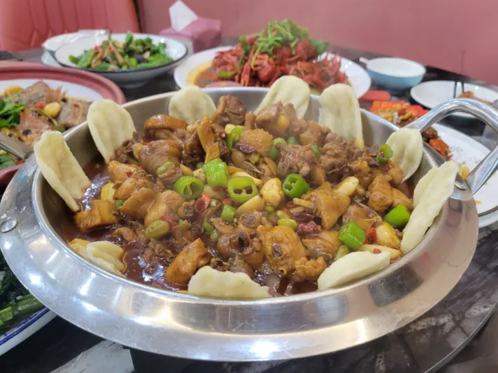 Pot of braised chicken pieces with chili and flatbread wedges around the rim