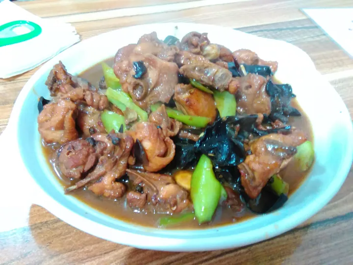 A plate of braised chicken pieces with black wood ear mushroom and green pepper in a rich brown sauce