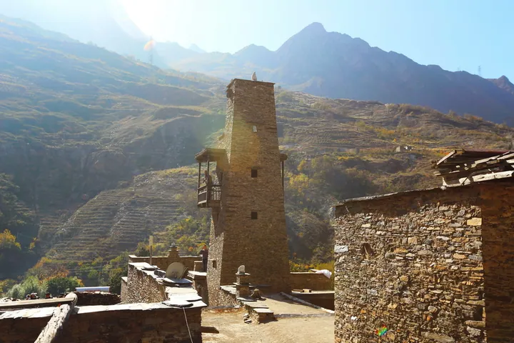 Traditional stone Qiang watchtower rising above stone houses in Taoping Qiang Village, with mountains in the background