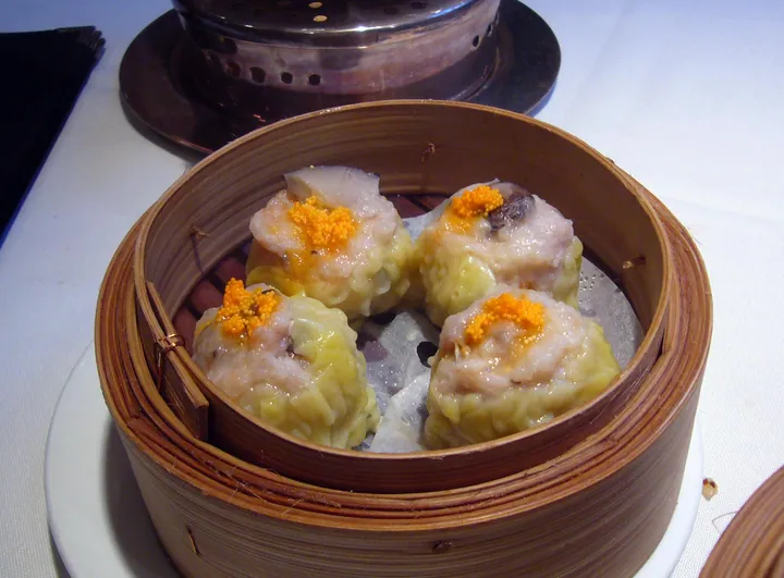 Four steamed shumai dumplings in a bamboo steamer