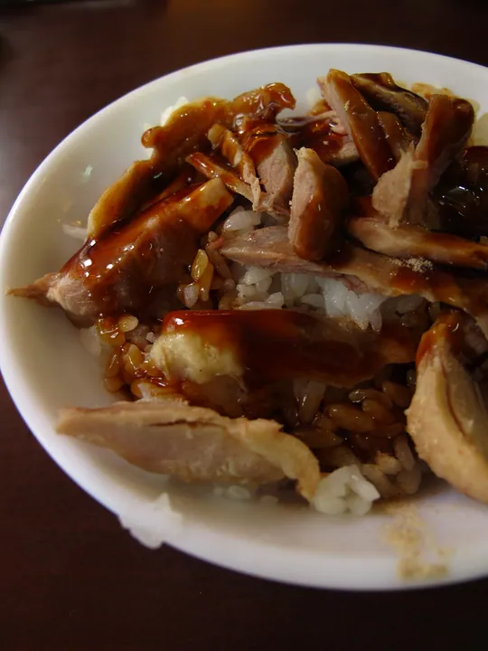 Sliced duck meat with brown sauce served over a bowl of rice