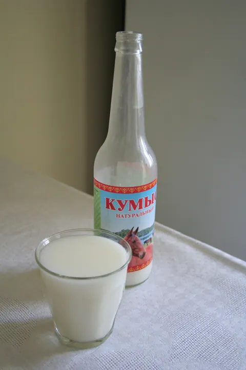 A glass and labeled bottle of white kumis, a fermented mare's milk drink