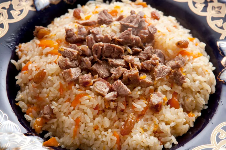 A plate of Xinjiang pilaf (shou zhua fan) with rice, mutton, carrot and raisins