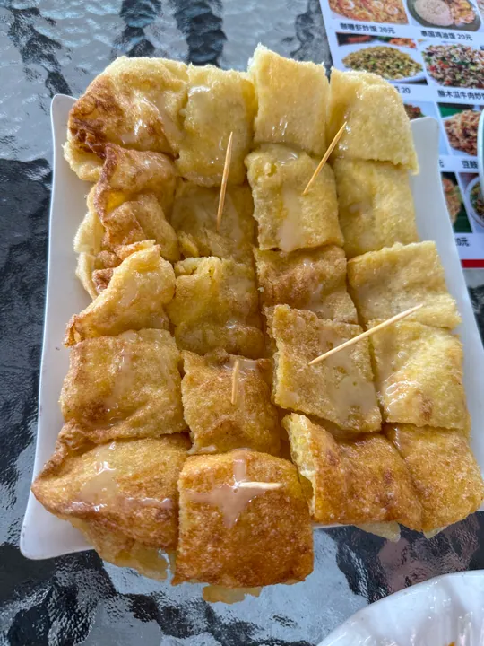 A plate of golden fried pastry squares drizzled with syrup