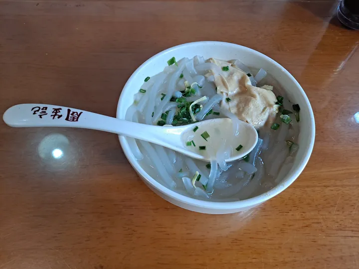 Bowl of tofu-skin wrapped dumplings in broth garnished with scallion