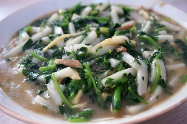 Plate of stir-fried white rice cake strips mixed with leafy greens