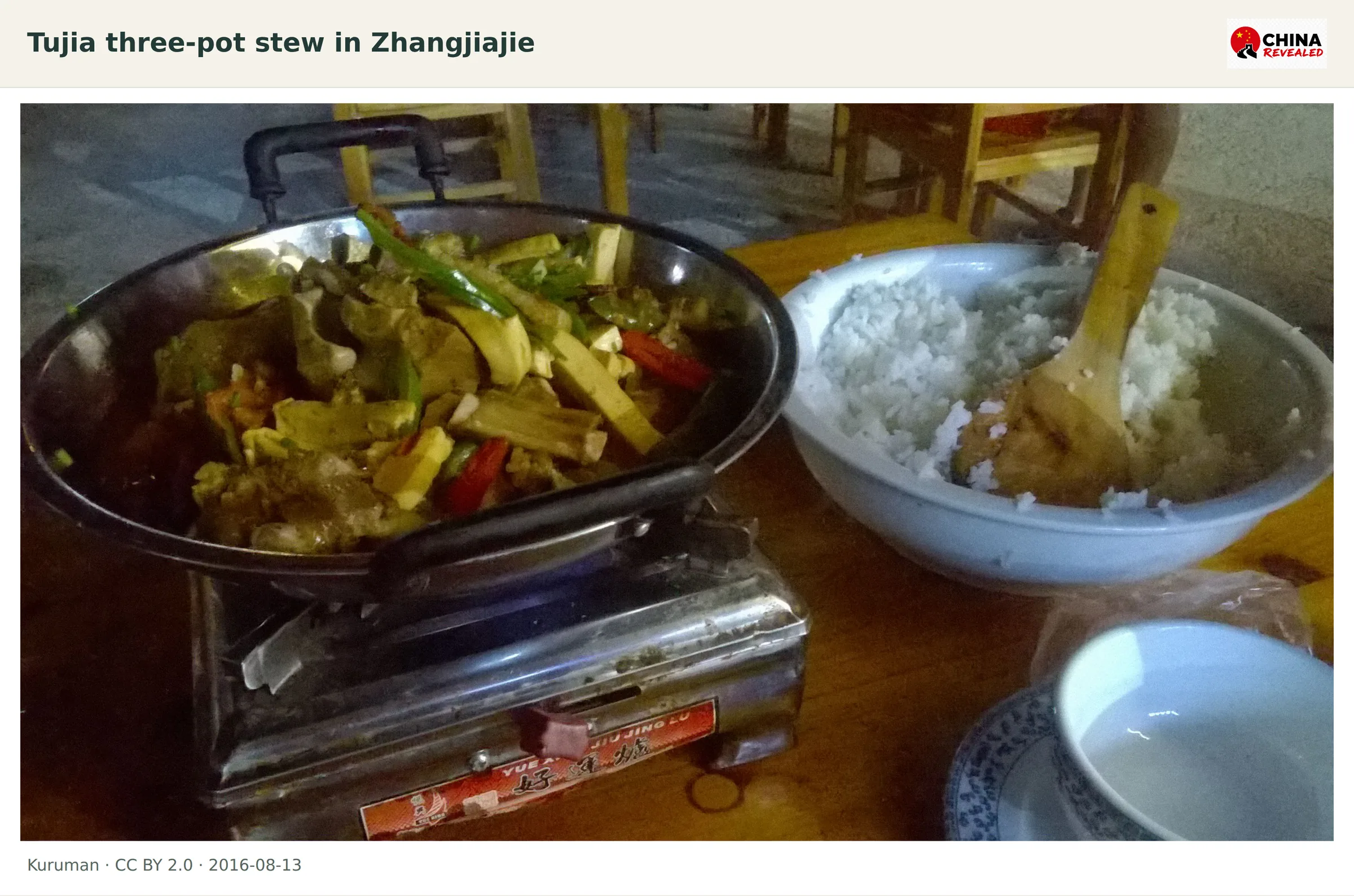 A metal pan of Tujia three-pot stew beside a bowl of rice at a Zhangjiajie meal